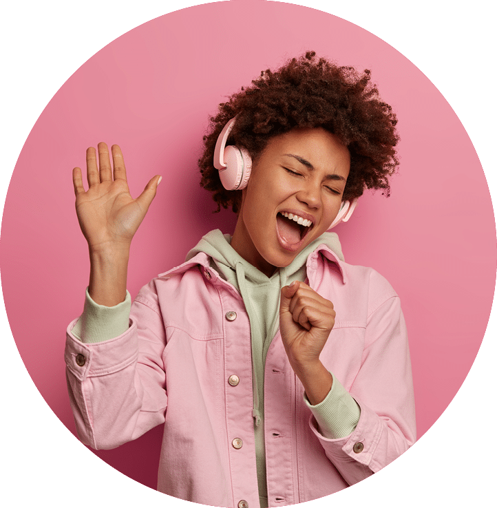 Photo of overjoyed woman sings along in headphones, makes microphone with hand, raises palm and dances carefree, being in positive mood, moves with rhythm of music, wears fashionable clothes