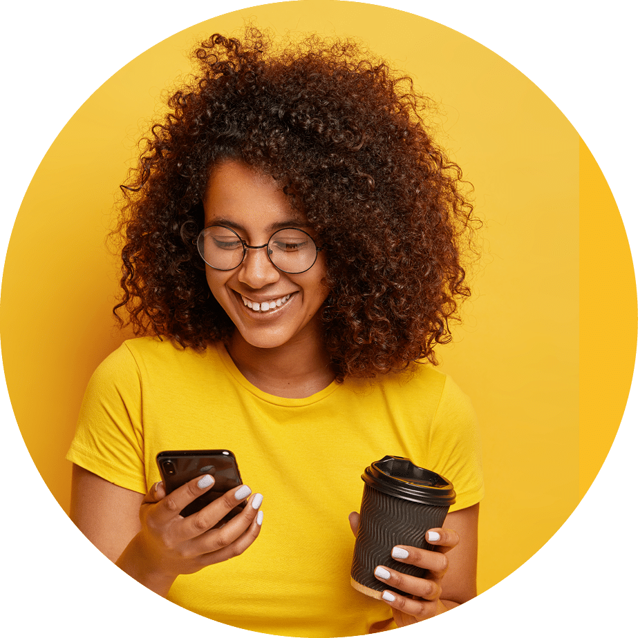 Happy teenage girl with curly hair, holds modern mobile phone, takeout coffee, orders taxi via online application, types text message, wears yellow clothing  People, modern lifestyle and technology
