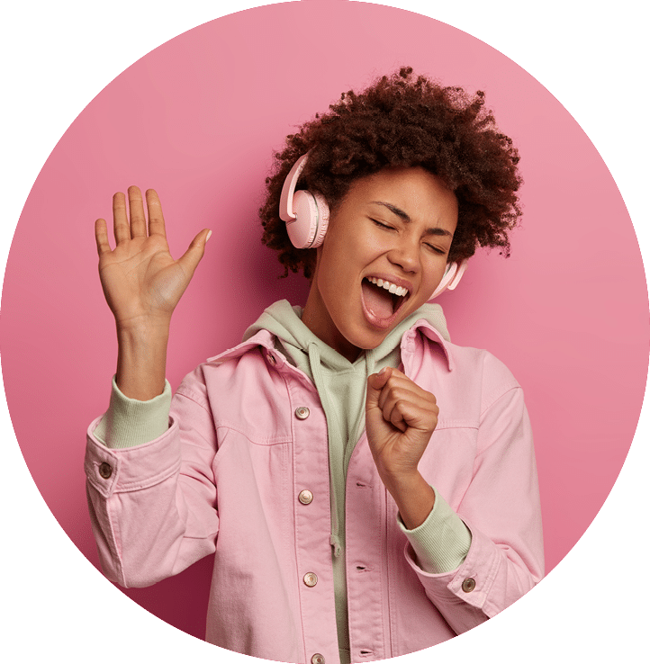 Photo of overjoyed woman sings along in headphones, makes microphone with hand, raises palm and dances carefree, being in positive mood, moves with rhythm of music, wears fashionable clothes